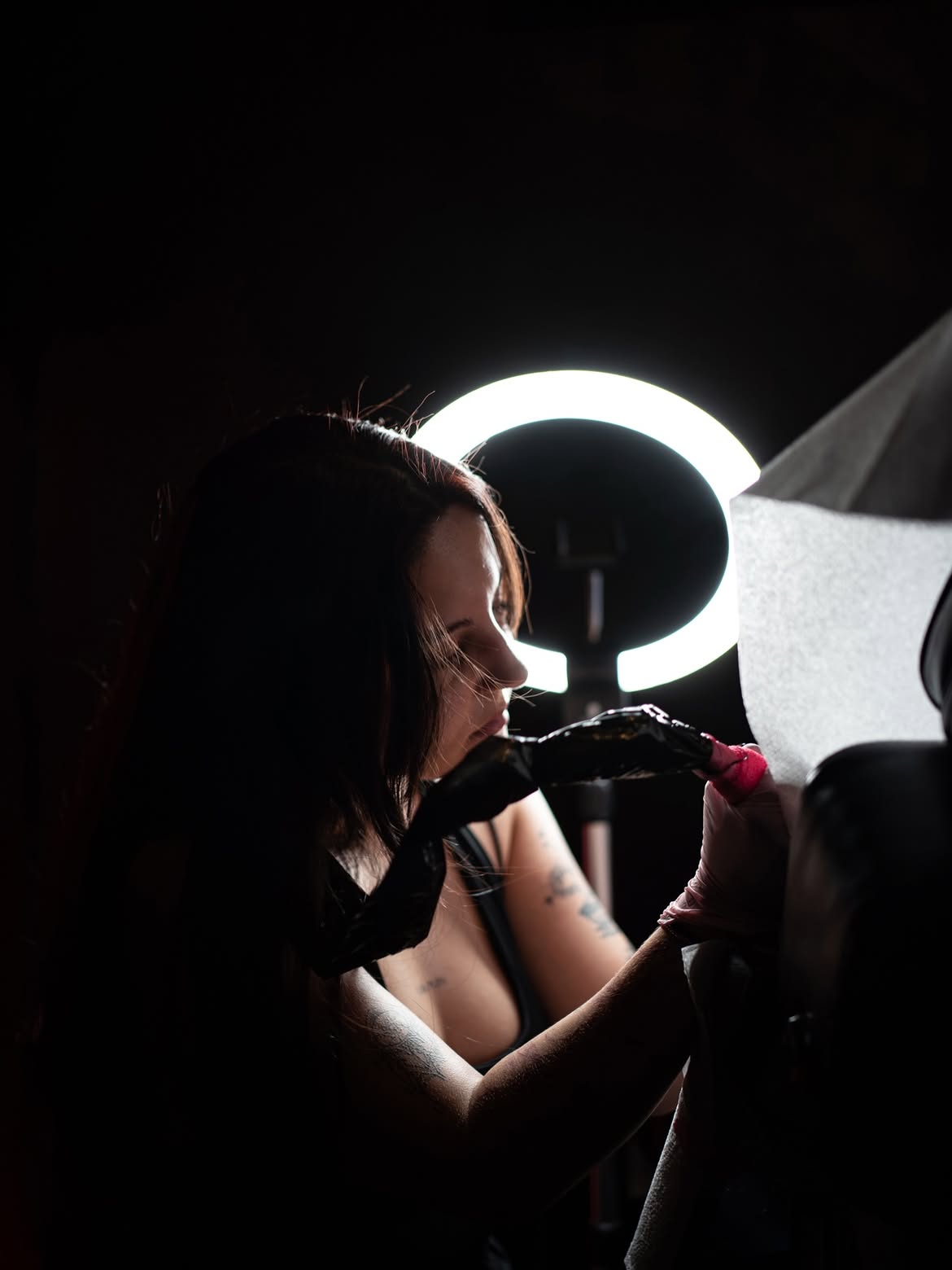 Simone en train de tatouer, concentrée, sous la lumière d'un ring light